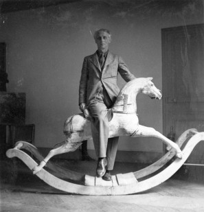 Schwarz-Weiß-Fotografie von Max Ernst auf einem Schaukelpferd.