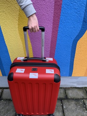 Ein roter Koffer vor einer bunten Hauswand